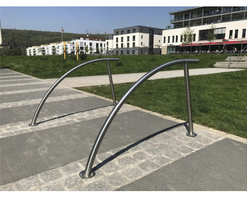 Zwei gebogene Edelstahl Fahrradbügel auf einem gepflasterten Platz.