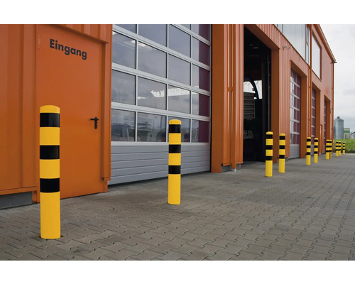 Bornes de protection anti-collision jaunes et noires devant un bâtiment industriel avec portes et porte d''entrée