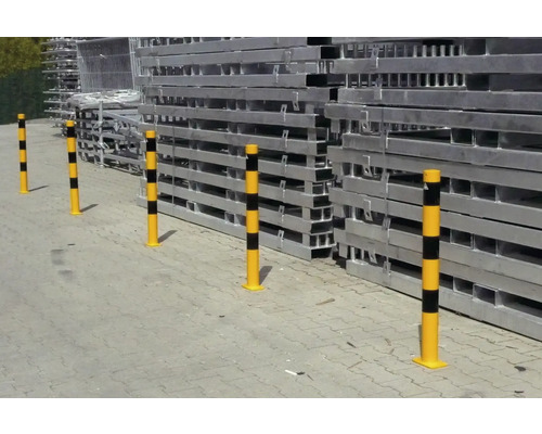 Plusieurs bornes de protection jaunes à rayures devant une pile d’éléments d’échafaudage