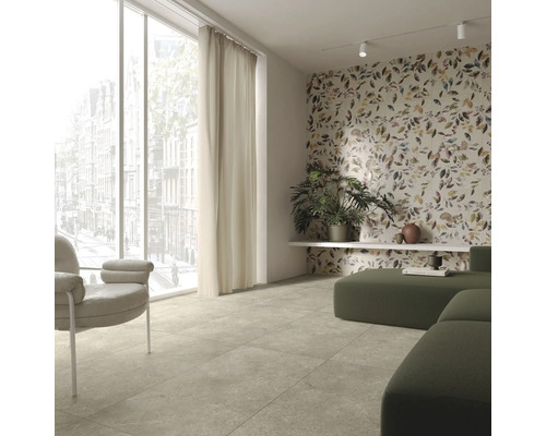 Salon lumineux avec sol carrelé, fenêtre, rideau, fauteuil, canapé modulable et revêtement mural à motifs végétaux.