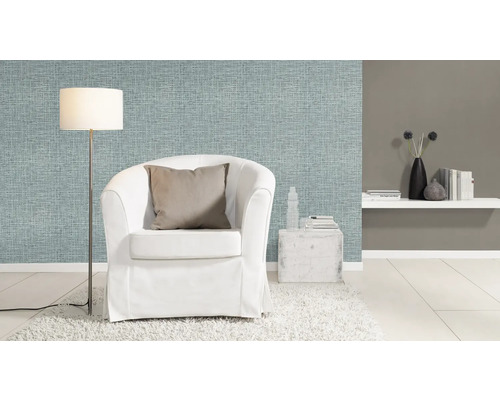 Salon avec papier peint textile bleu clair, fauteuil blanc et lampadaire.