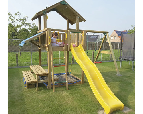 Kind auf Holzspielturm mit Rutsche, Schaukel und Sandkasten im Garten