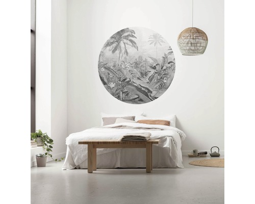Chambre avec papier peint rond sur le thème de la jungle au-dessus du lit, table en bois et suspension en rotin