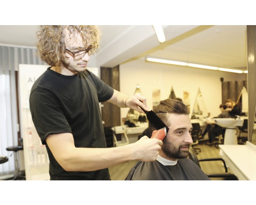 Ein Friseur schneidet einem Kunden mit einem Haarschneider die Haare.