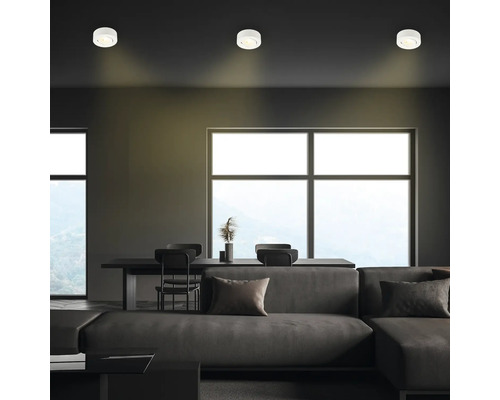 Wohnzimmer mit Deckenleuchten, Sofa, Tisch und Stühlen.