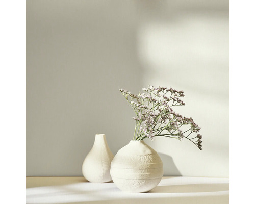 Zwei weisse Vasen, eine mit Trockenblumen, auf einem hellen Untergrund.