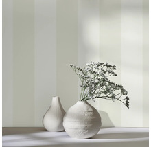 Deux vases blancs avec des fleurs séchées devant un papier peint à rayures