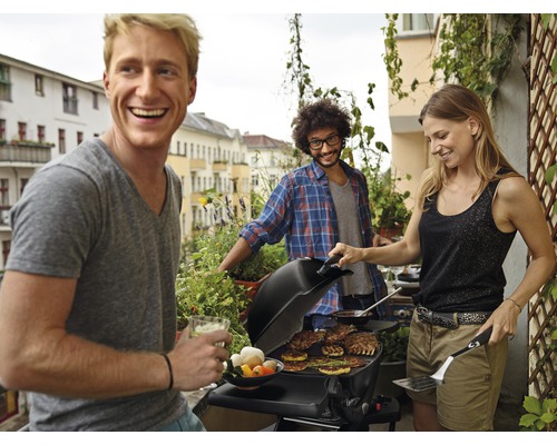 Freunde grillen zusammen auf einem Balkon mit einem Gasgrill.