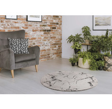 Salon avec fauteuil gris, tapis rond et plantes d''intérieur devant un mur en briques.