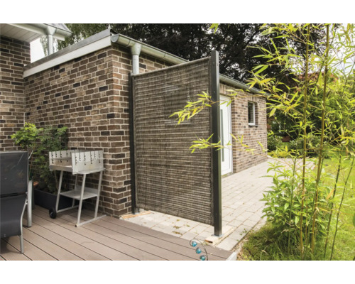 Extérieur avec paravent, barbecue et mobilier de jardin sur une terrasse devant un bâtiment en briques.