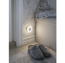 Scène avec une veilleuse ronde à LED avec détecteur de mouvement fixée au mur, des chaussons et un tapis