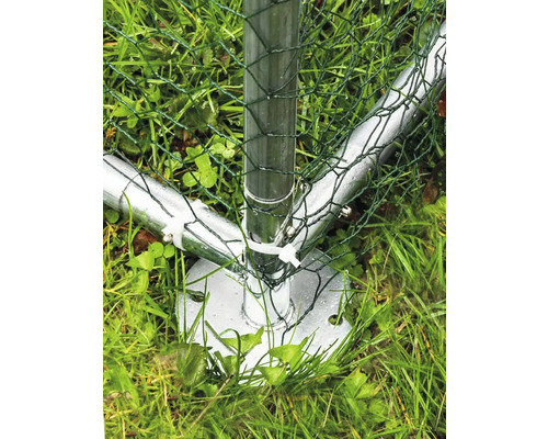 Gros plan d''un poteau de clôture métallique avec un grillage vert dans l''herbe.