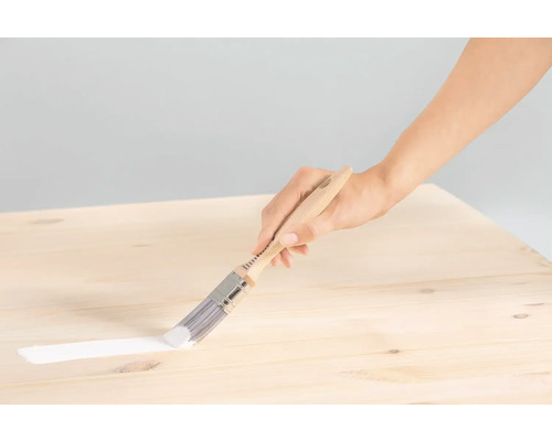 Eine Person streicht mit einem Pinsel eine Holzoberfläche