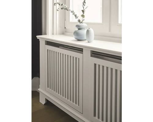 Cache-radiateur en bois avec des lamelles verticales et deux vases sur le dessus.