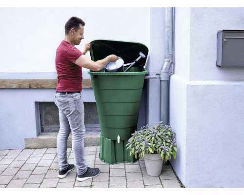 Mann befüllt eine Regentonne mit Giesskanne und Eimer.