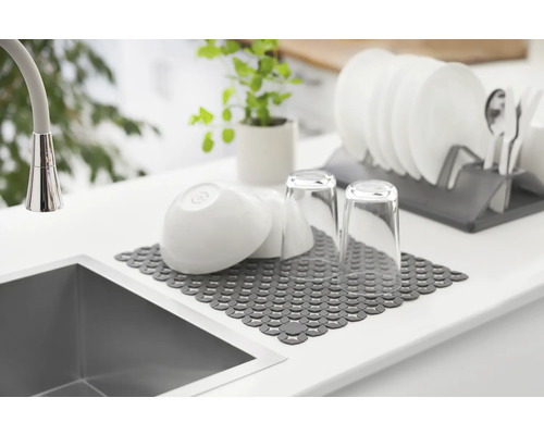 Spüle mit Abtropfmatte, Geschirr und Gläsern auf einer Küchentheke.