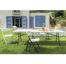 Szene im Freien mit einem weißen Gartentisch und passenden Stühlen auf einer Rasenfläche vor einem Haus.