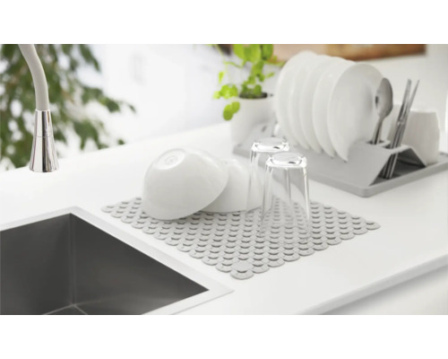 Spüle mit Abtropfmatte, Geschirr und Geschirrkorb auf einer Arbeitsfläche.