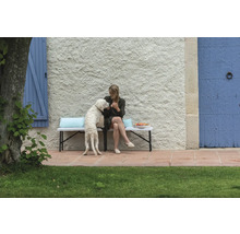 Femme avec chien sur un banc de jardin devant un mur de maison