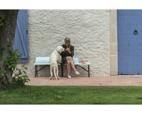 Femme avec chien sur un banc de jardin devant un mur de maison