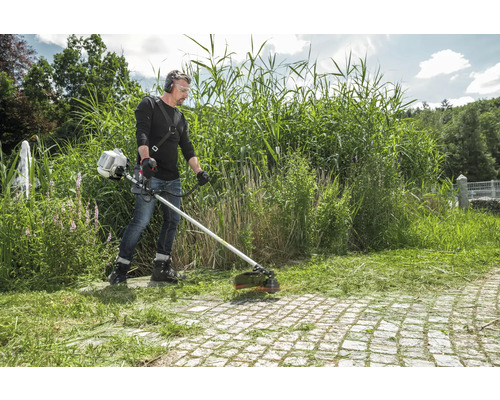 Mann schneidet Gras mit einem Freischneider im Garten.