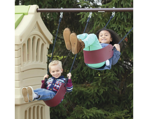 Deux enfants se balancent sur une balançoire devant une tour de jeux.