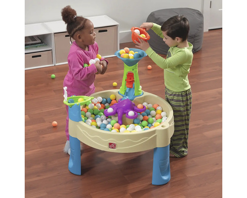 Deux enfants jouent avec une table de jeu et des balles colorées.