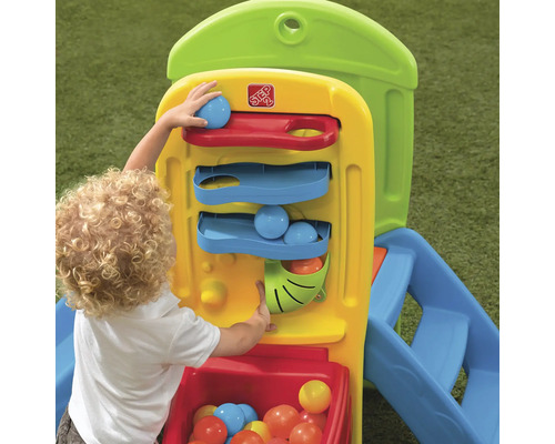 Enfant joue avec la maisonnette Step2 avec toboggan et balles.