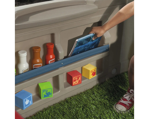 Vue détaillée d''une cabane de jeu avec des compartiments de rangement pour les jouets et un enfant rangeant un carnet.