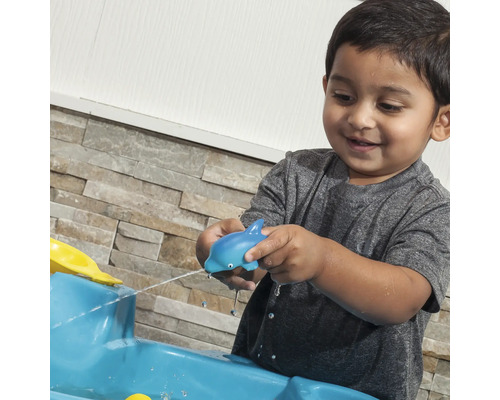 Un enfant joue avec un dauphin bleu, jouet aquatique, sur une table d''eau bleue.