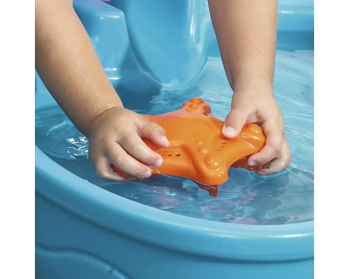 Un enfant joue avec une étoile de mer orange dans une pataugeoire bleue.