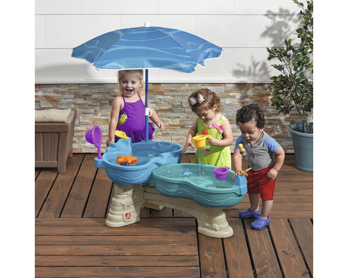Des enfants jouent à une table de jeu d''eau avec un parasol à l''extérieur.