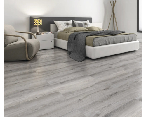 Chambre claire avec sol stratifié imitation bois, lit, fauteuil et table de chevet