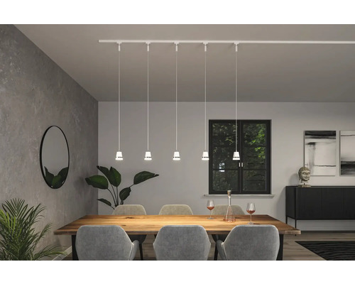 Salle à manger avec table, chaises, plantes d''intérieur, miroir, buffet, décoration et un rail d''éclairage blanc avec cinq suspensions.