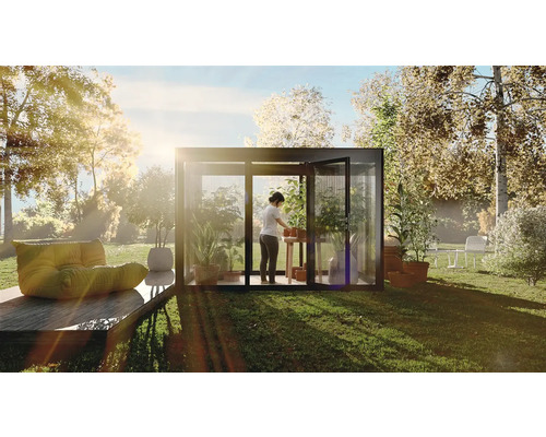 Une serre dans le jardin avec une personne rempotant des plantes sur une table, entourée de verdure et d''arbres.