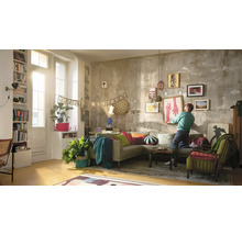 "Wohnzimmer mit Sofa, Sesseln, Pflanzen und einer Person, die ein gerahmtes Bild an einer Wand mit verschiedenen Kunstwerken aufhängt. Eine Girlande mit der Aufschrift ""Happy Birthday"" ist ebenfalls zu sehen."