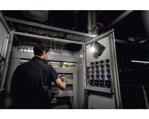 Électricien travaillant sur une armoire électrique avec une lampe fixée