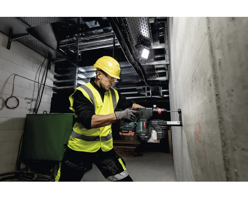 Un homme perce un trou dans un mur de béton avec un marteau perforateur sur un chantier.