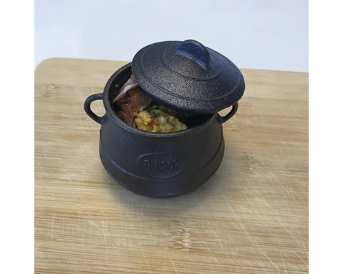 Schwarzer Topf aus Gusseisen mit Deckel und Speisen auf einem Holzbrett