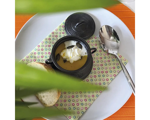 Suppe mit Kürbiskernen in einem kleinen Topf mit Deckel, dazu Brot und ein Löffel auf einem Teller