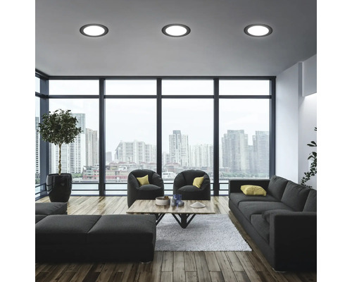 Modernes Wohnzimmer mit Sofa, Sesseln, Tisch und Deckenleuchten vor Fensterfront mit Stadtblick