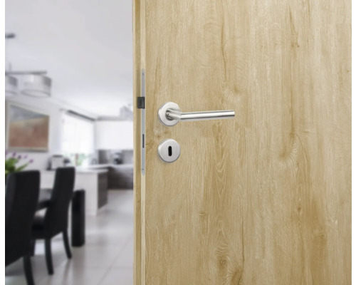 Porte intérieure ouverte avec poignée de porte et serrure devant une salle à manger et une cuisine