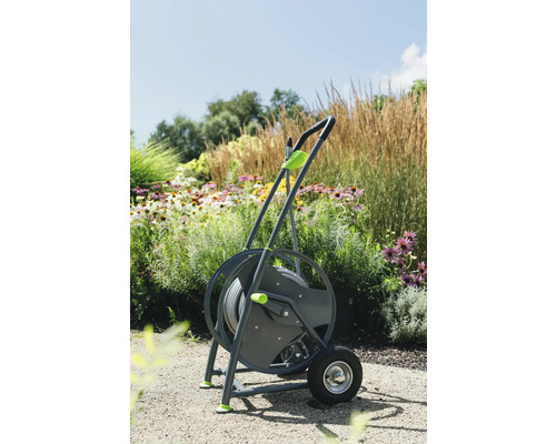 Dévidoir sur roues avec tuyau d''arrosage devant parterre de fleurs