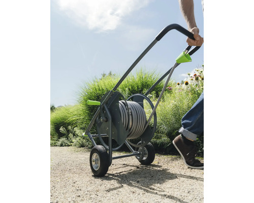 Une personne tire un chariot à tuyau avec un tuyau d''arrosage dans le jardin.