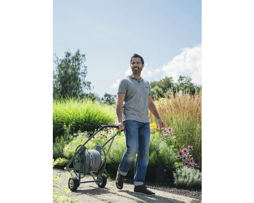 Un homme tire un chariot de tuyau d''arrosage dans un jardin.