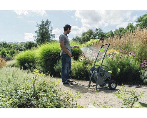 Un homme arrose un jardin avec un dévidoir.