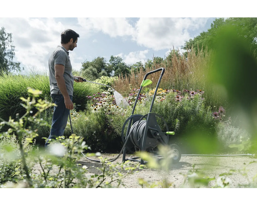 Un homme arrose des fleurs avec un tuyau d''arrosage, le tuyau est enroulé sur un chariot dévidoir.