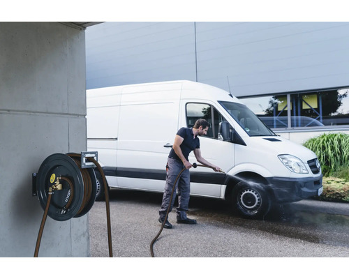 Un homme nettoie un camion avec un enrouleur de tuyau fixé à un mur en béton