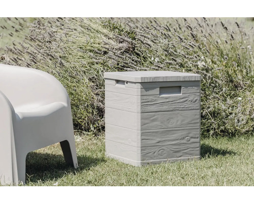 Aufnahme einer grauen Gartenbox mit Holzoptik und einem Hocker auf einer Rasenfläche.