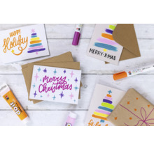 Plusieurs cartes de Noël avec des crayons de couleur et un emballage sur une table.